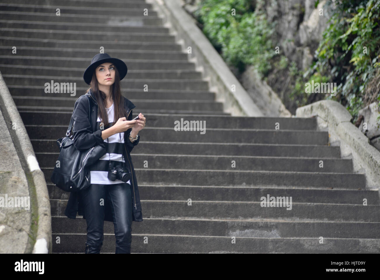 Tourist (Frau) Treppen hinunter in Budapest, gekleidet in schwarzem Leder mit Fotokamera und Hut Stockfoto