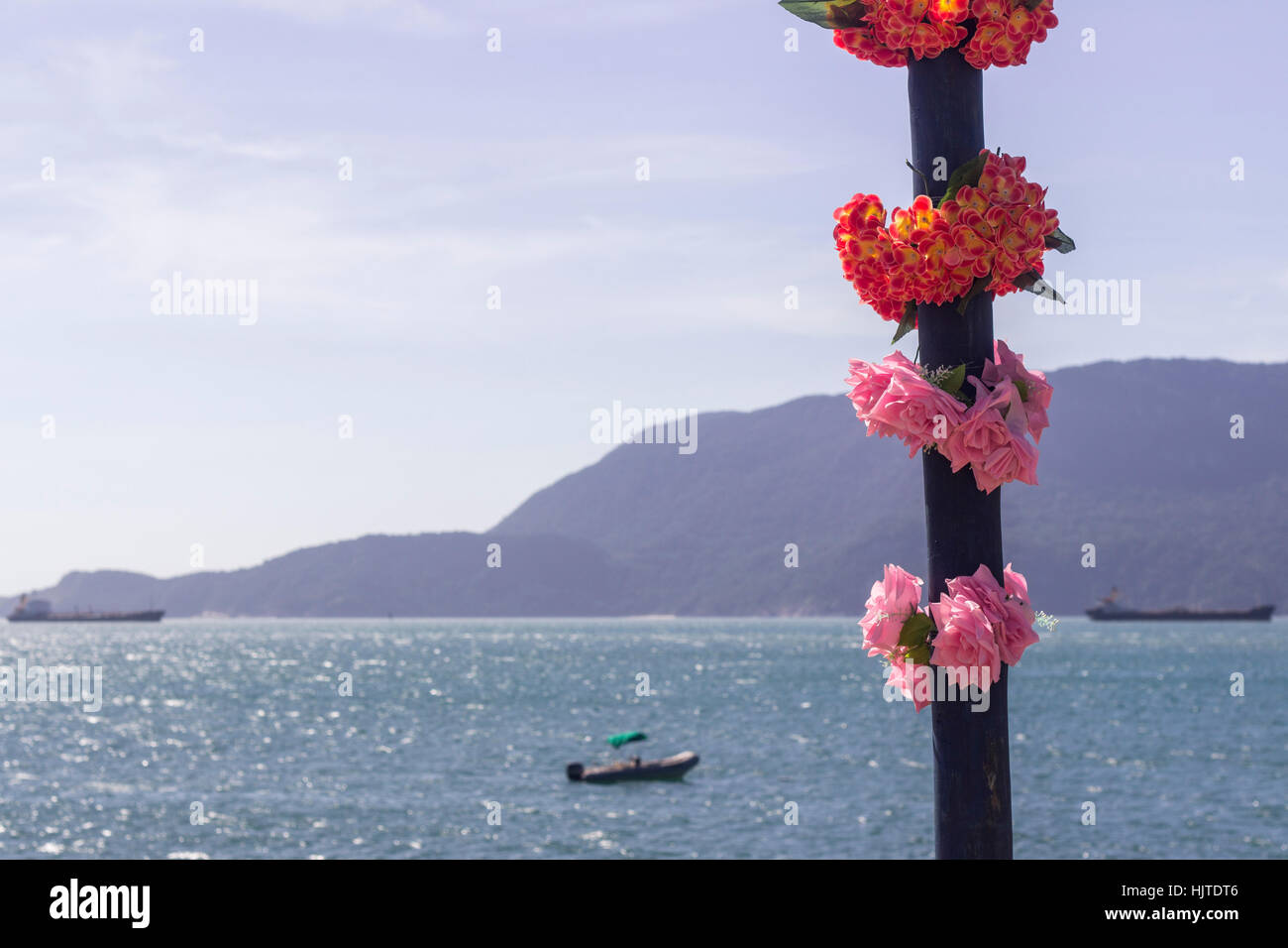 Ilhabela, Bundesstaat Sao Paulo, Brasilien, künstliche Blumen auf einen Beitrag über Praia Grande mit Meer und Bergen im Hintergrund Stockfoto