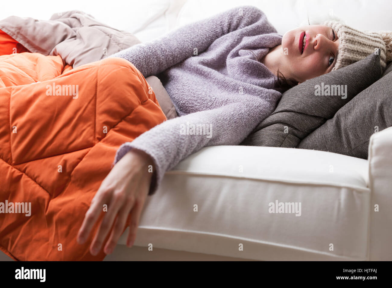Frau liegt auf einem Sofa in einer pathetischen Pose mit einer starken Grippe und affig Hut Stockfoto
