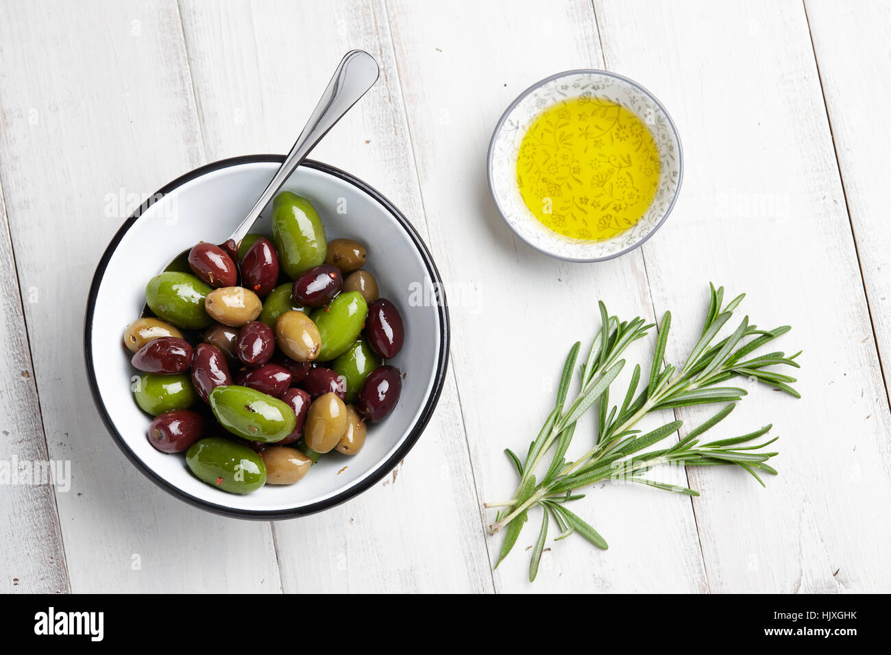 Frischen Oliven Mix, Zweige Rosmarin und Olivenöl auf weißem Holz Hintergrund Stockfoto
