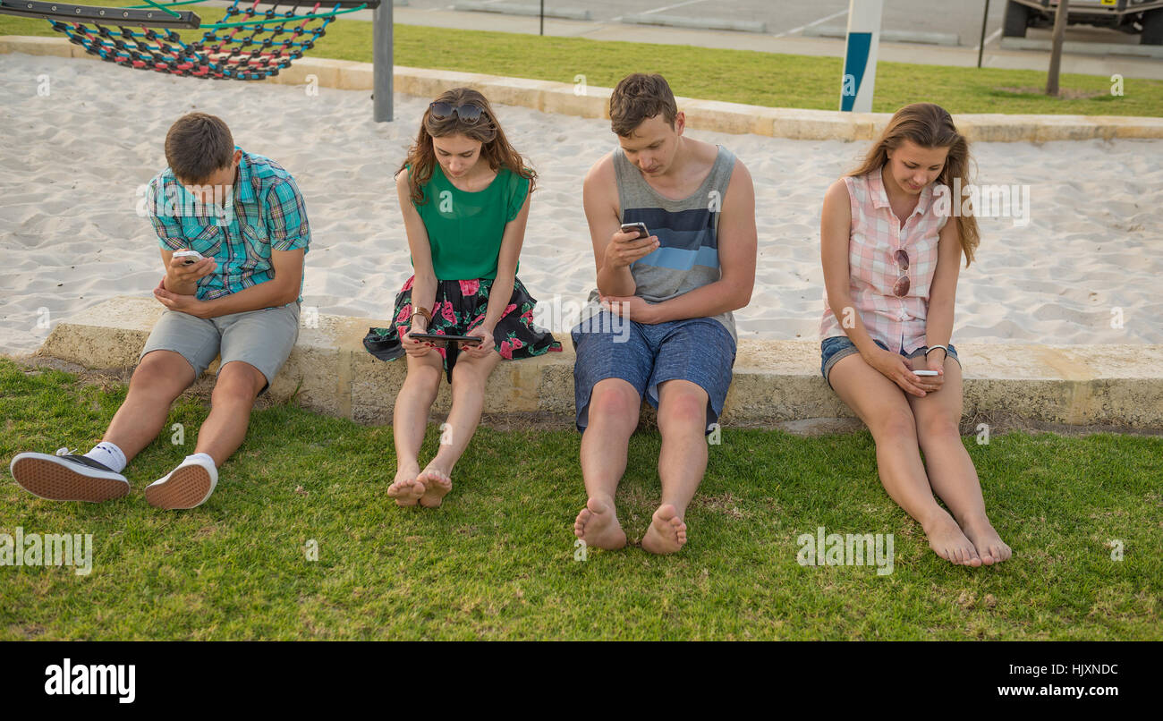 Gruppe von Jugendlichen mit ihren digitalen Geräten im Freien im Abendlicht. Konzept der drahtlosen Kommunikation und verlieren reales Stockfoto