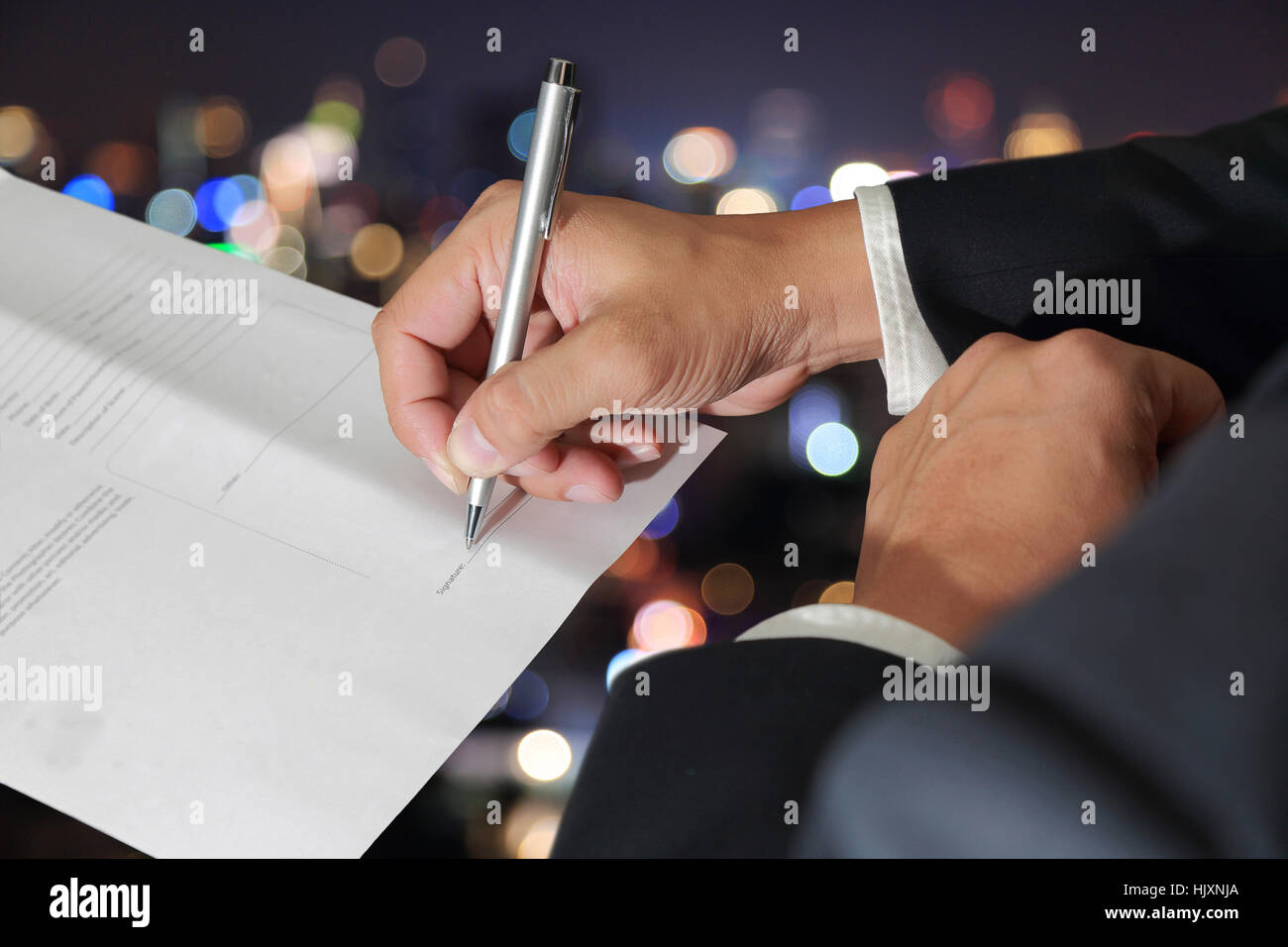 Das Unternehmer Hand hält einen Stift Unterzeichnung des Dokuments auf unscharfe abstrakte Nacht Bokeh Hintergrund als Genehmigung Konzept. Stockfoto