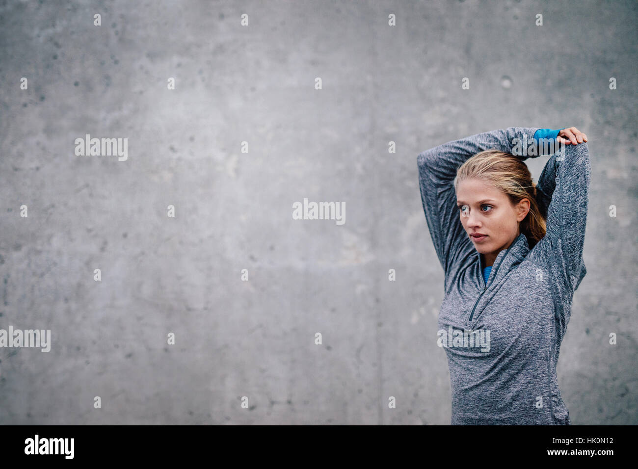Weibliche Läufer streckte die Arme nach einer laufenden Sitzung. Junge sportliche Frau vor grauem Hintergrund wegsehen. Stockfoto