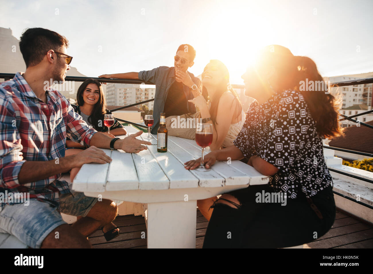 Gruppe von jungen Leuten an einem Tisch mit Getränken. Junge Männer und Frauen, die auf dem Dach Abend feiern. Stockfoto