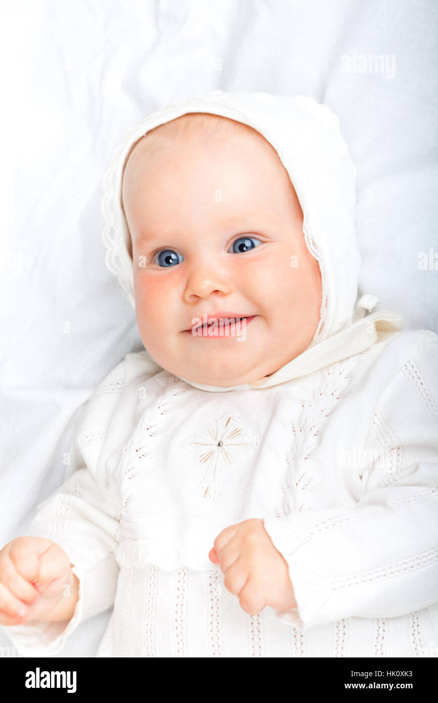 Nahaufnahme der sechsmonatigen Babymädchen tragen weiße Taufe Kleidung Verlegung auf einem Bett lächelnd Stockfoto