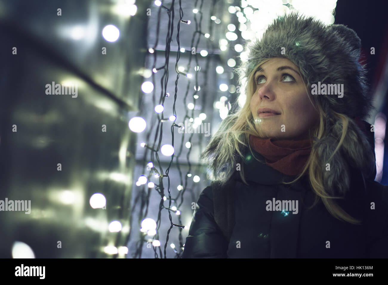 Kaukasische blonde Frau gekleidet für den Winter beobachten die dekorative uteten üge auf einer Gebäudewand Stadt Nachtszene Stockfoto