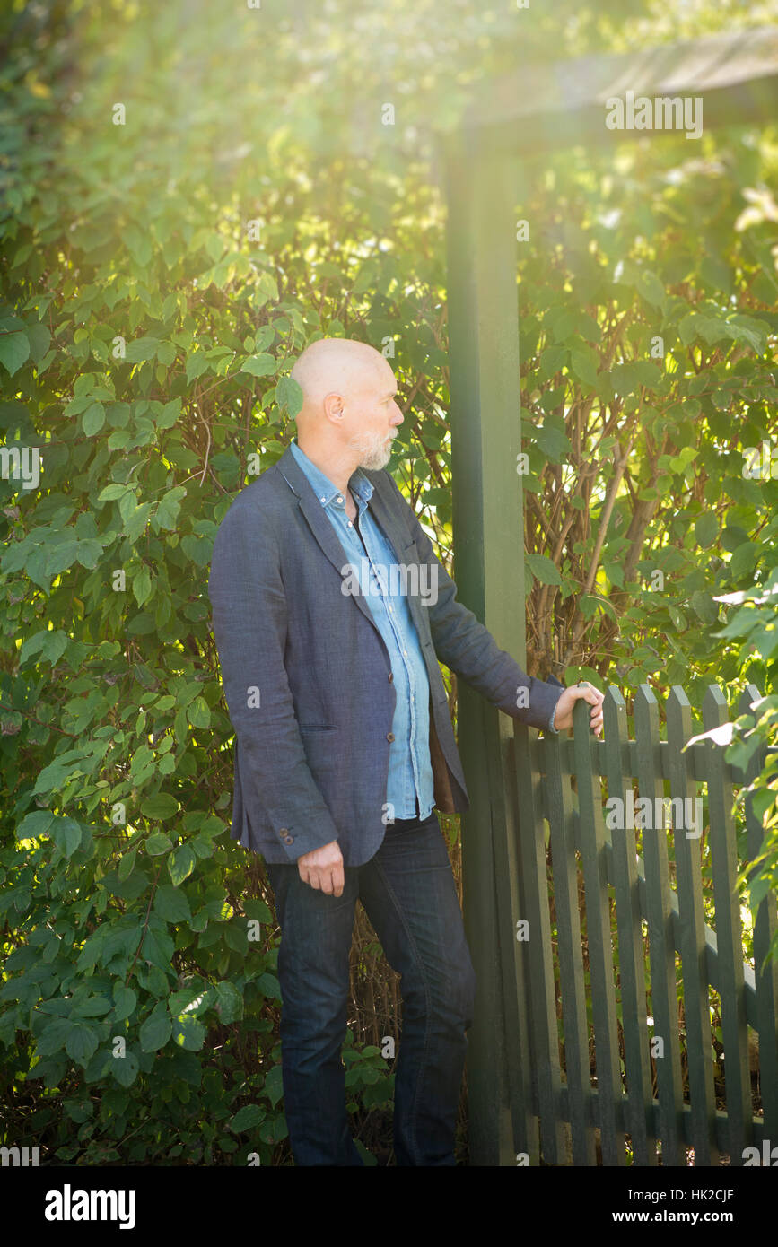 Alter Mann durch Gartentor warten. Sommer Lifestyle Moment der älteren Person. Stockfoto