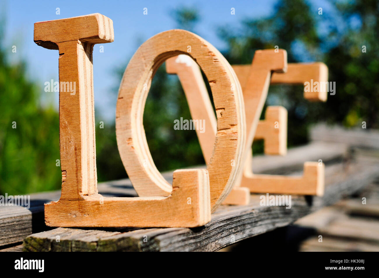 einige dreidimensionale Holzbuchstaben bilden das Wort Liebe, platziert auf einer verwitterten Holzoberfläche im Außenbereich, mit Bäumen im Hintergrund Stockfoto