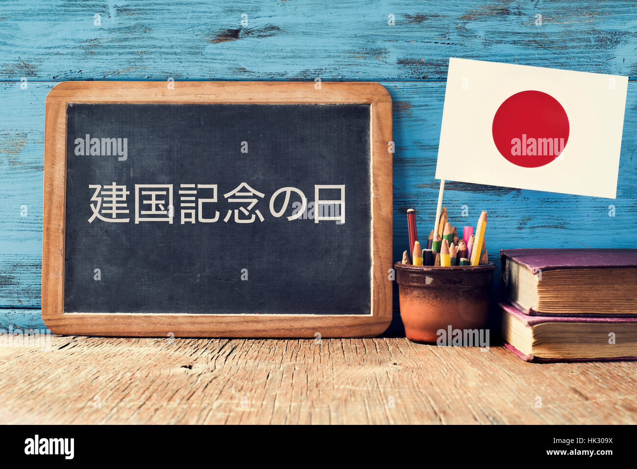 eine Tafel mit dem Text National Foundation Day in Japanisch, einen Topf mit Bleistiften, einige Bücher und die Flagge von Japan, auf einem rustikalen hölzernen Schreibtisch geschrieben Stockfoto