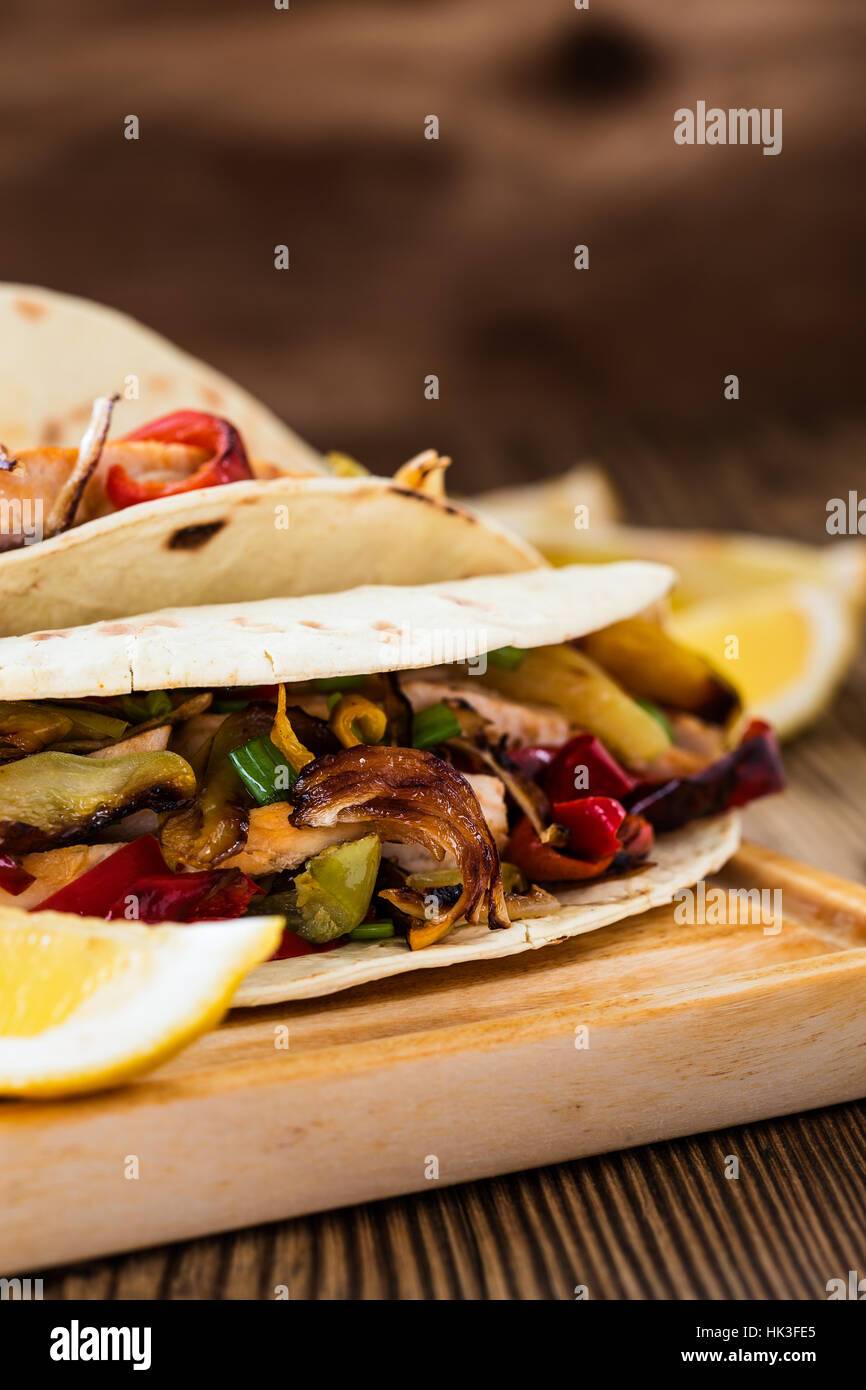 Chicken Sie Fajitas mit gegrillten Zwiebeln und Paprika und mit Mehltortillas auf ländlichen Holzbrett servieren Stockfoto