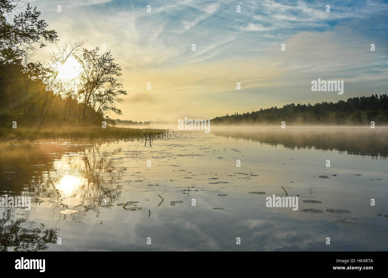 Brillante und leuchtende Mitte Sommer Sonnenaufgang an einem See.   Warmes Wasser und kühlere Luft bei Tagesanbruch schafft nebligen Nebelschwaden.  Stilles Wasser auf ruhigen Gewässern. Stockfoto