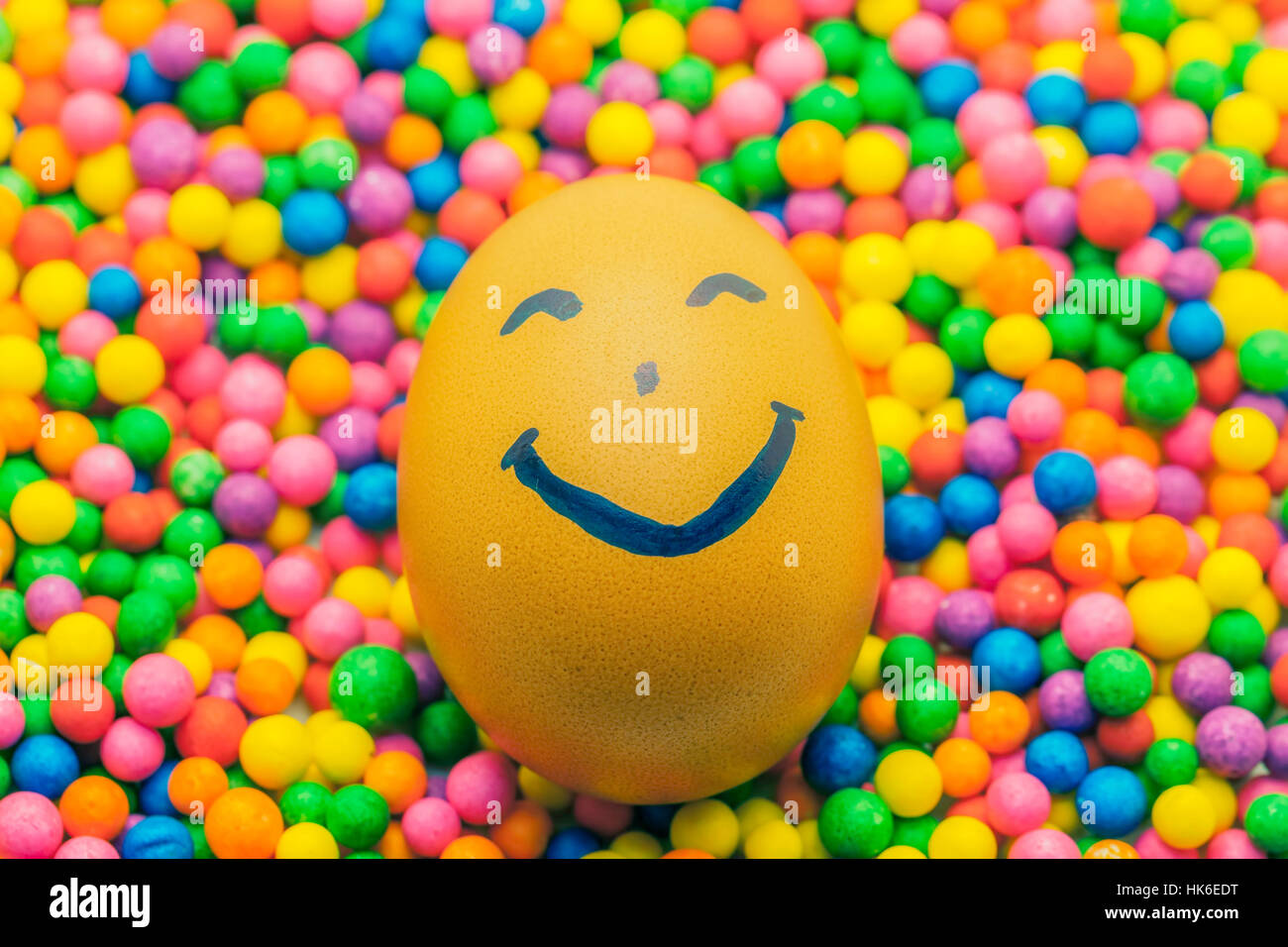 Braune Hühner Ei glückliches Gesicht auf dem bunten Hintergrund voller Bonbons und Konfetti Stockfoto