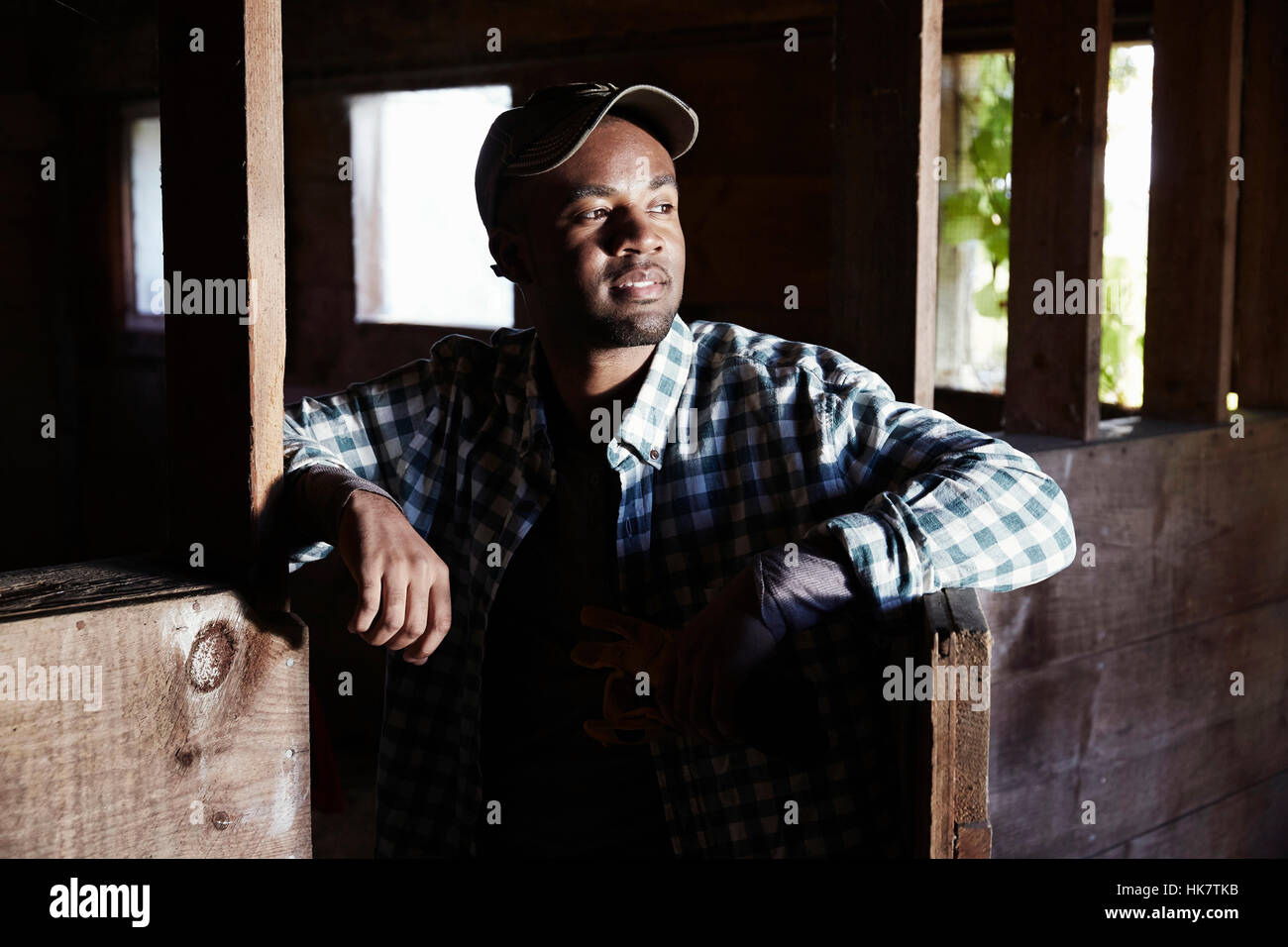 Ein junger Mann in Arbeitskleidung in einem hölzernen Wirtschaftsgebäude stehen. Stockfoto