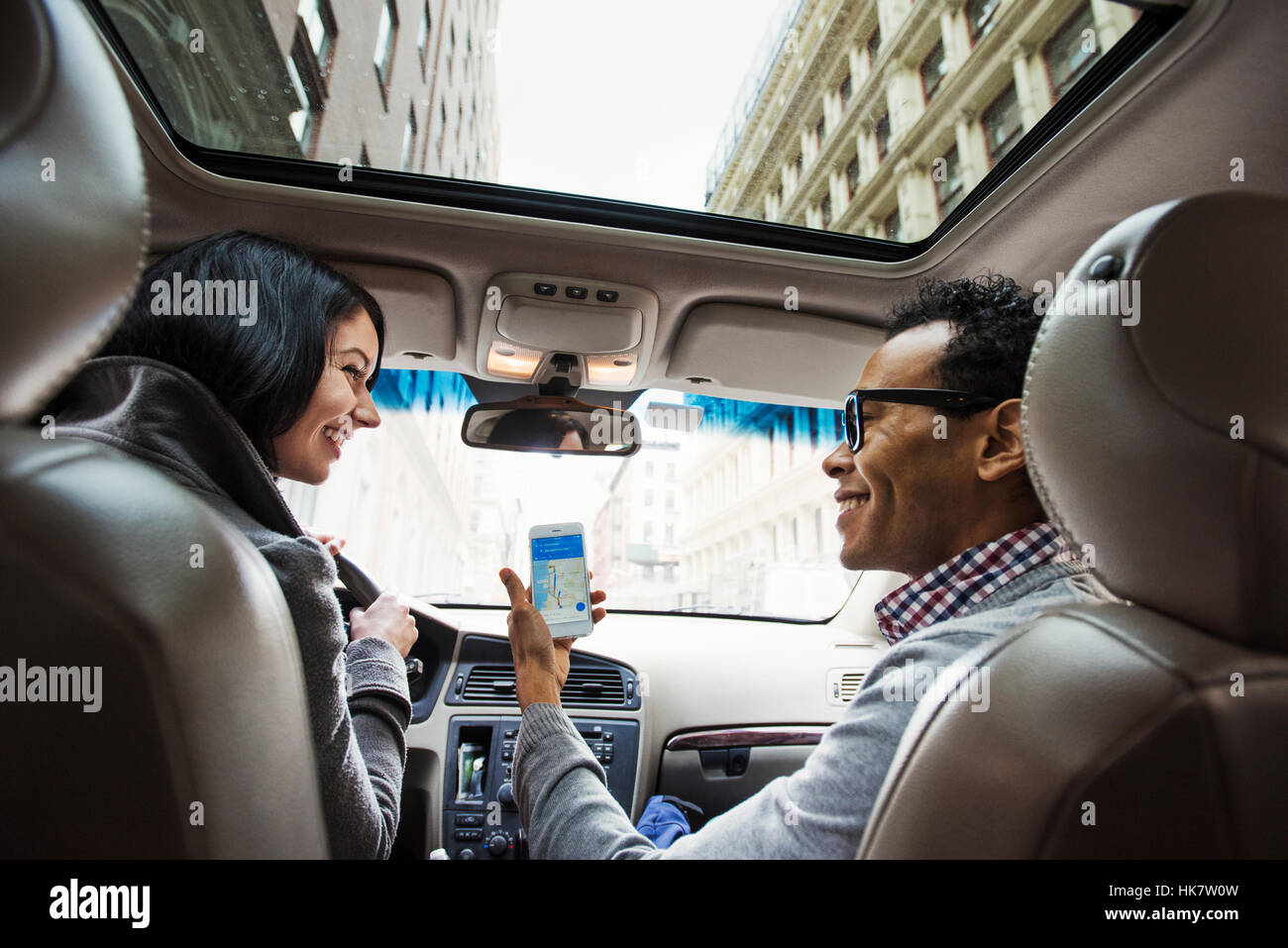 Eine junge Frau und ein junger Mann in einem Auto Blick auf eine Karte auf dem Display eines Handys, gesehen von der Rückbank. Stockfoto