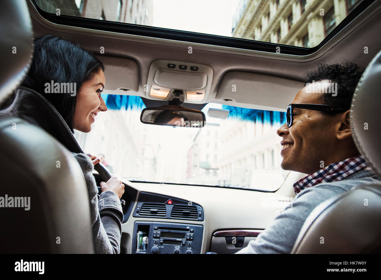 Eine junge Frau und ein junger Mann in einem Auto schauen einander an und Lächeln, gesehen von der Rückbank. Stockfoto
