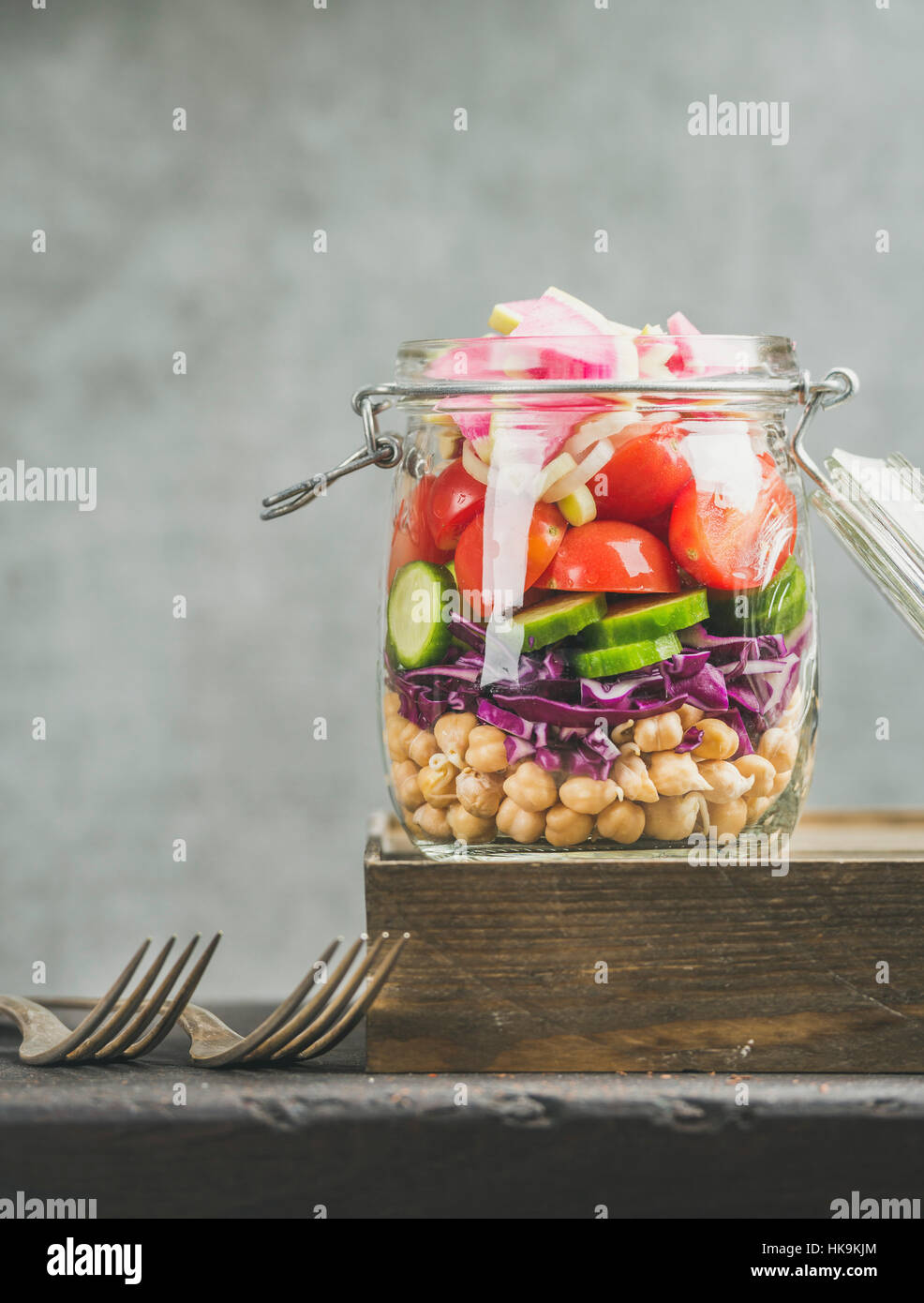 Gesundes Mittagessen zum Mitnehmen-Glas. Gemüse und Kichererbsen sprießen geschichteten vegane Salat im Glas Glas, graue Betonwand Hintergrund, Textfreiraum, selektive focu Stockfoto