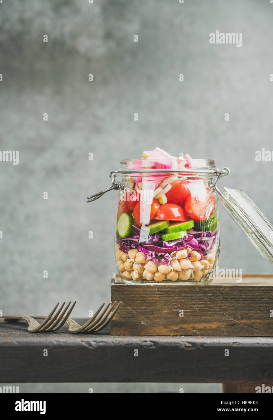 Gesundes Mittagessen zum Mitnehmen-Glas. Gemüse und Kichererbsen sprießen geschichteten vegane Salat im Glas Glas, graue Betonwand Hintergrund, Textfreiraum, selektive focu Stockfoto