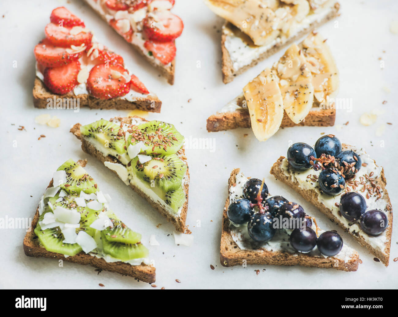 Gesundes Frühstück Vollkorn Brot Toast mit Frischkäse, verschiedenen Früchten, Samen und Nüssen. Draufsicht, grauer Marmor Hintergrund. Sauber, Essen, vegetarisch Stockfoto