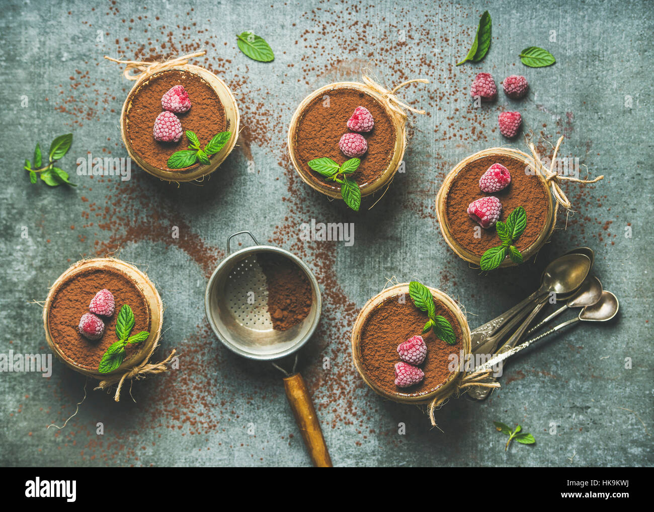 Hausgemachte italienisches Dessert Tiramisu in einzelnen Gläsern mit Minze serviert Blätter, Himbeeren und Kakaopulver über graue konkreten Hintergrund, Ansicht von oben, Stockfoto