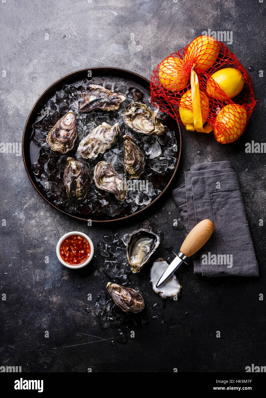 Austern in Platte mit pikanter Sauce und Zitrone auf dunklen Stein Textur Hintergrund Textfreiraum Stockfoto