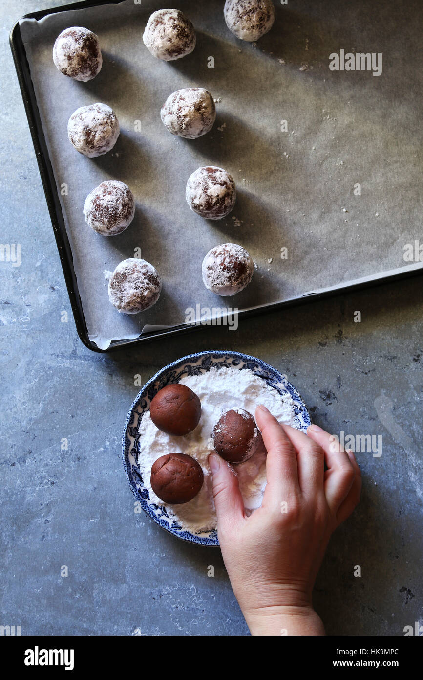 Machen Schokolade Crinkle Cookies. Weibliche Hand Beschichtung Teig Kugel mit Puderzucker bestreuen. Ansicht von oben Stockfoto