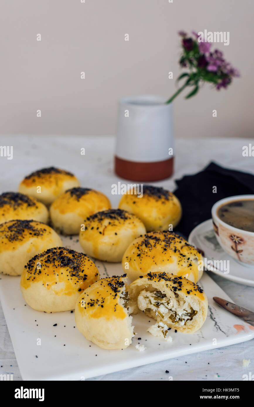 Türkische Brötchen gefüllt mit Feta und Petersilie serviert auf einem Brett, einer von ihnen ist halbiert und begleitet von einer Tasse Kaffee und eine Blume. Stockfoto