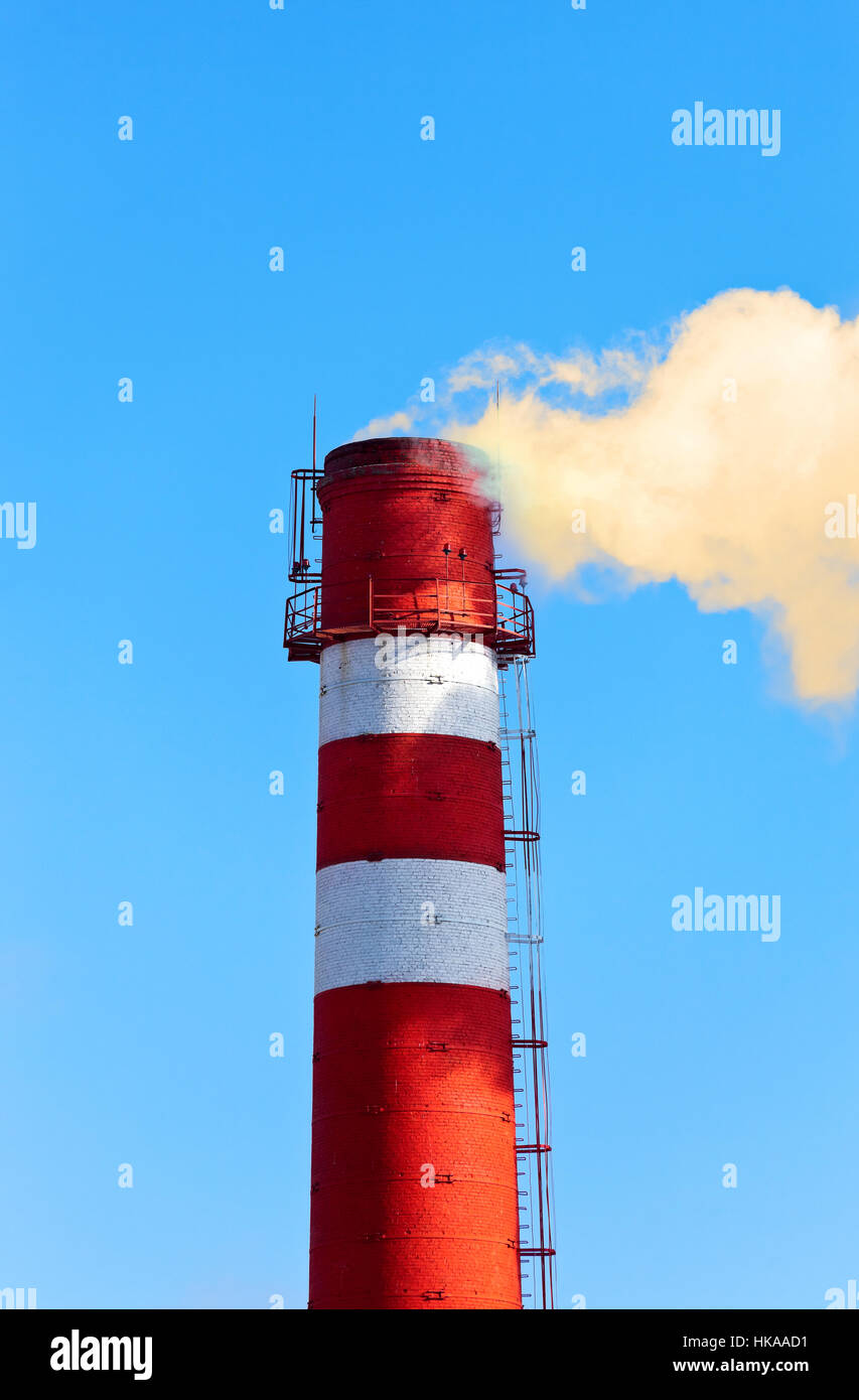 Rote und weiße Fabrikschlot mit Rauch gegen blauen Himmel Stockfoto