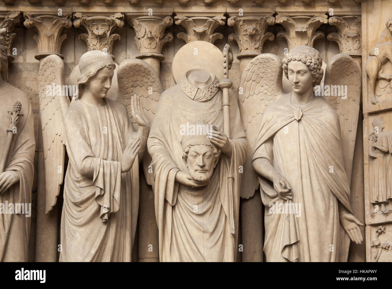Saint-Denis (Dionysius) hält er den Kopf und von Engeln umgeben. Neo-gotische Statue an der Hauptfassade der Kathedrale Notre-Dame (Notre-Dame de Paris) in Paris, Frankreich. Beschädigte gotische Statuen an der Hauptfassade wurden in den 1840er Jahren von französischen Architekten Eugene Viollet-le-Duc und Jean-Baptiste Lassus restauriert. Stockfoto