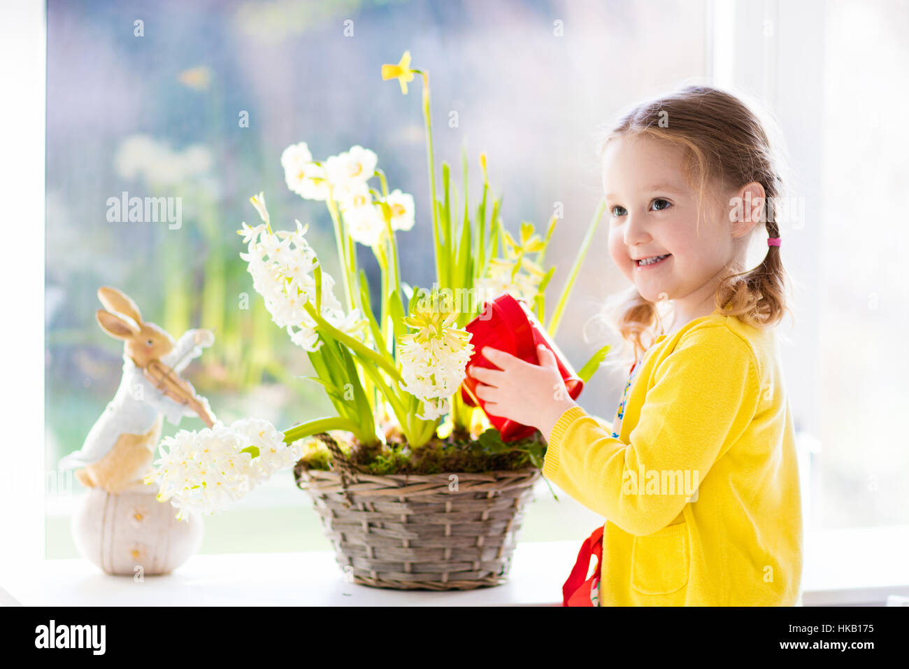 Niedliche Mädchen erste Frühlingsblumen gießen. Ostern-Wohngebäude und Dekoration. Kind kümmert sich um Pflanzen. Kind mit Wasser kann. Stockfoto