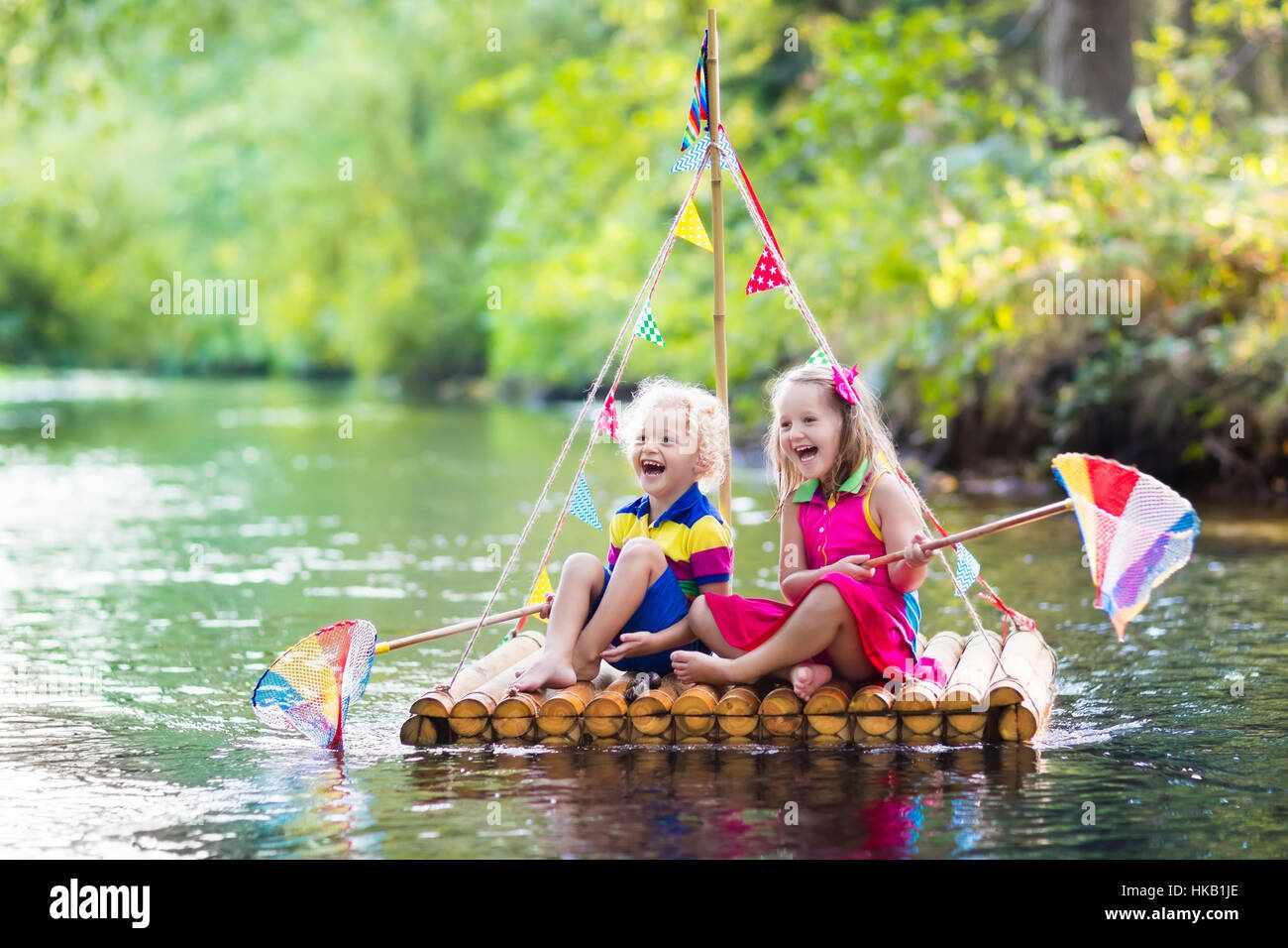 Zwei Kinder auf hölzerne Floß Fang von Fischen mit einem bunten Netz in einem Fluss und das Spiel mit Wasser am heißen Sommertag. Stockfoto