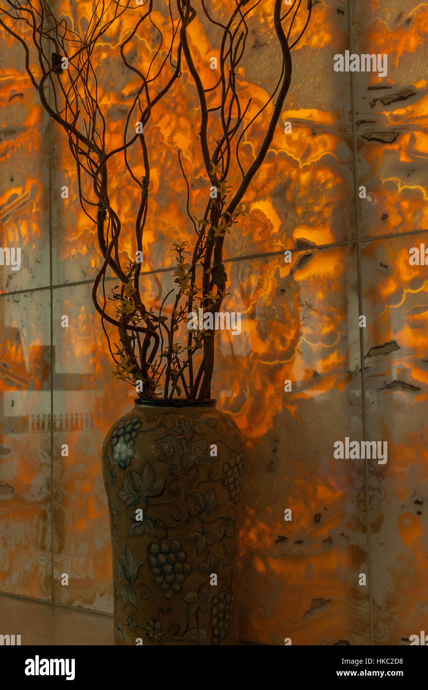 Ein großer dunklen farbigen Keramik Topf halten lange, dünne Gliedmaßen eines Baumes, einer flammenden orange Aquarell-ähnlichen Wand. Stockfoto