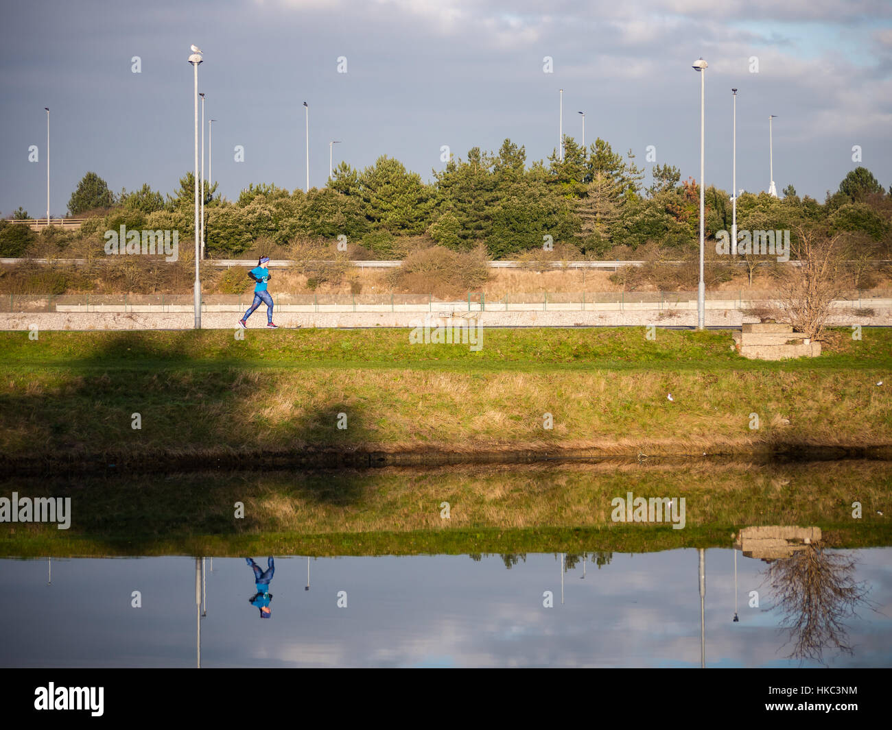 Ein weibliche Läufer läuft neben einem See ihr Spiegelbild im Wasser gießen Stockfoto