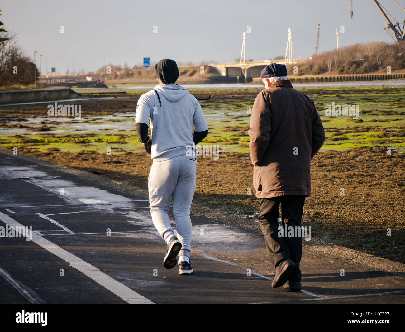Ein junger Mann Unternehmen einen Morgenlauf überholt einen Alter Mann aus seiner morgendlichen Spaziergang Stockfoto