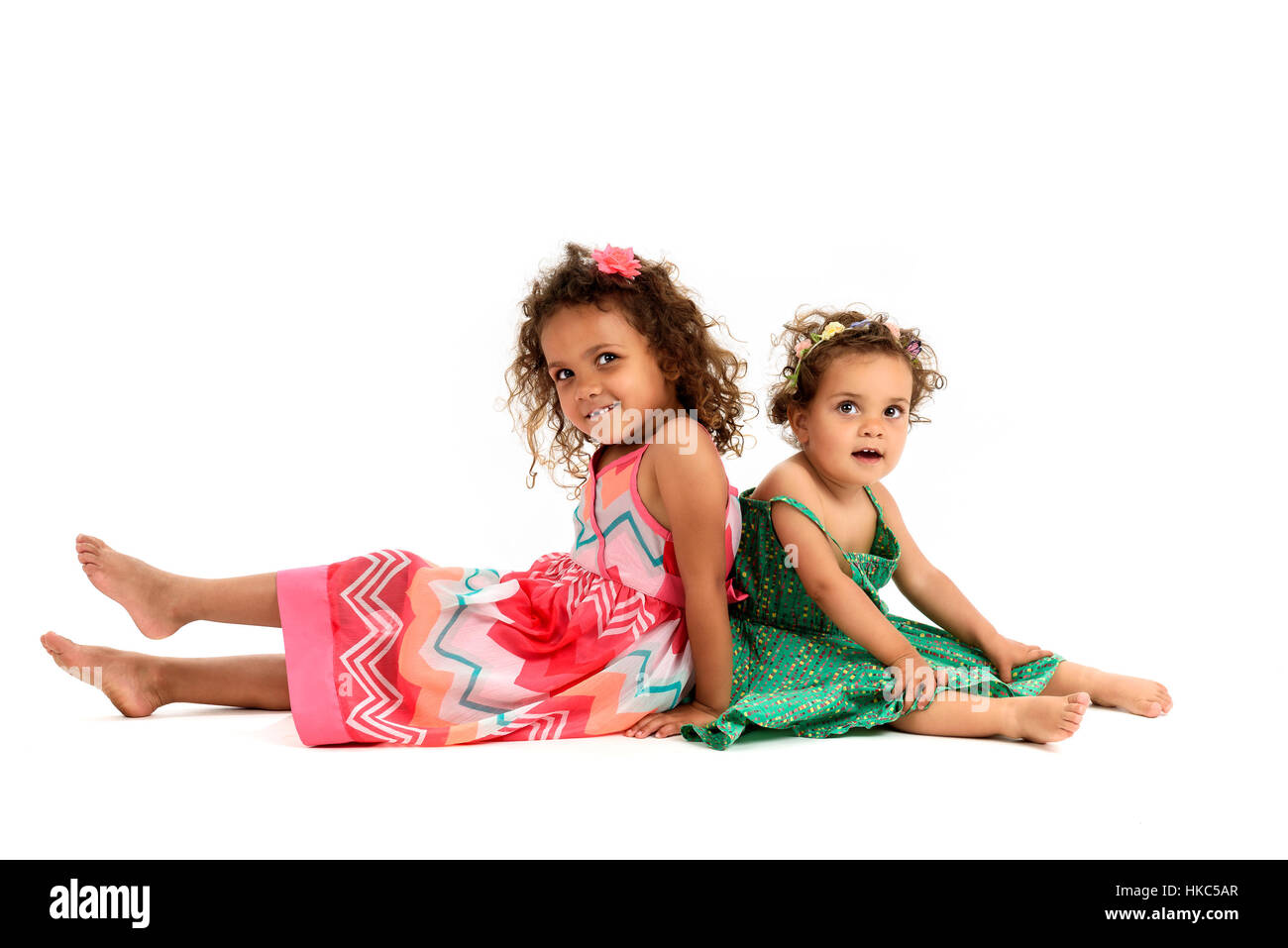 Mulatte Schwestern sitzen Rücken an Rücken zu spielen. Mädchen in roten und grünen Kleid spielen, lächelnd und zeigt Schwester Liebe und Glück. Eine Mädchen ist m Stockfoto