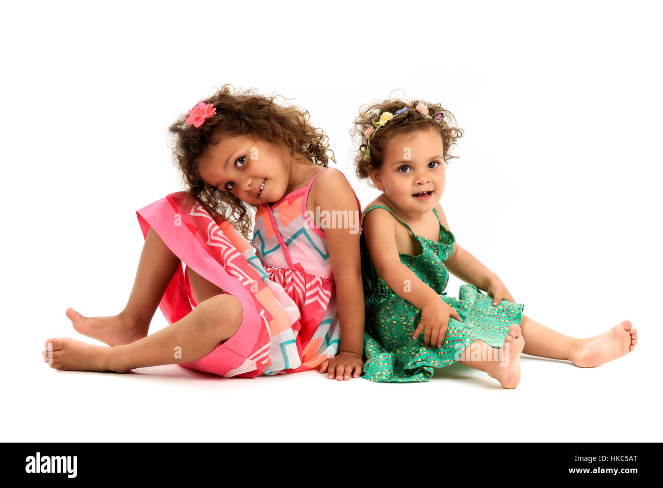 Mulatte Schwestern sitzen Rücken an Rücken zu spielen. Mädchen in roten und grünen Kleid spielen, lächelnd und zeigt Schwester Liebe und Glück. Eine Mädchen ist m Stockfoto