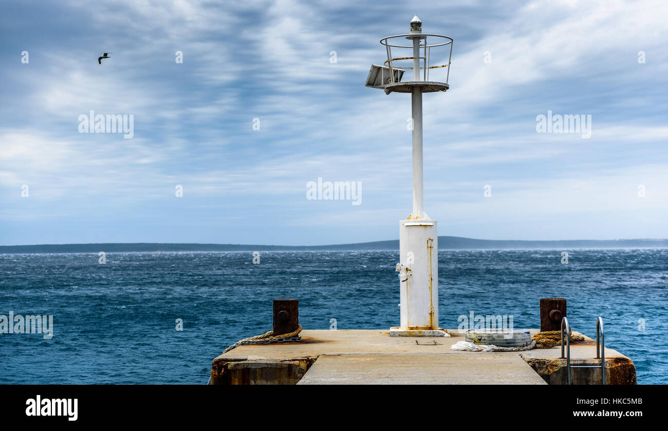 Alte Mole mit Leuchtturm Leuchtfeuer und ruhige See. Rostigen Verankerungen auf Betonpfeiler an einem windigen Tag mit dramatische Wolken. Adria - Insel Silba, Kroatien. Stockfoto