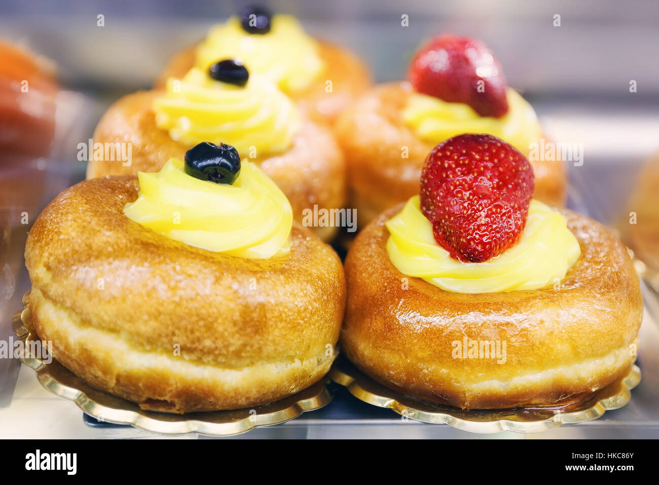 Zwei Baba, eins mit gelben Creme und schwarzen Kirschen, die andere gelbe Creme mit Erdbeeren. Stockfoto