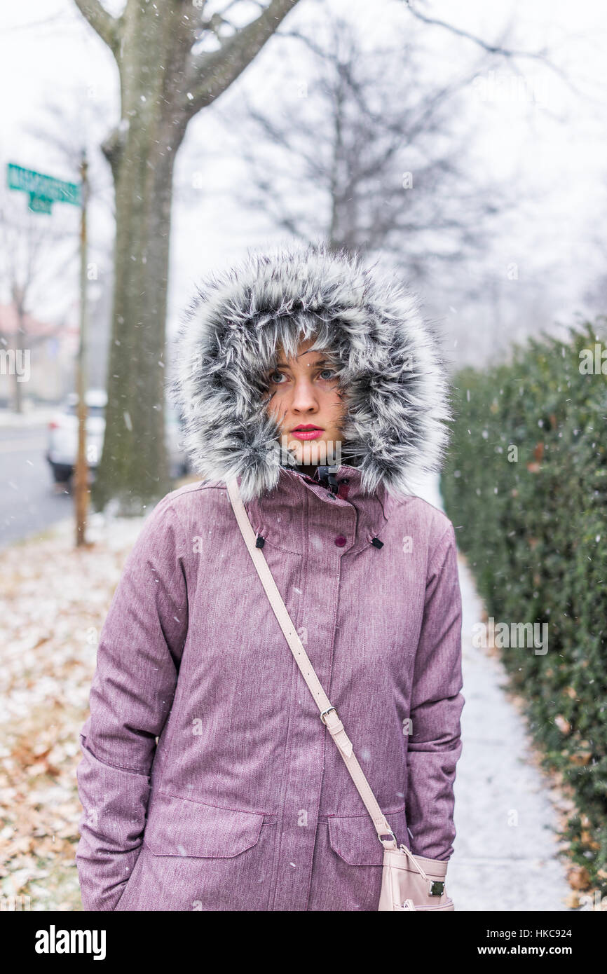 Junge Frau zu Fuß auf Bürgersteig in Mantel im Winterschnee Stockfoto