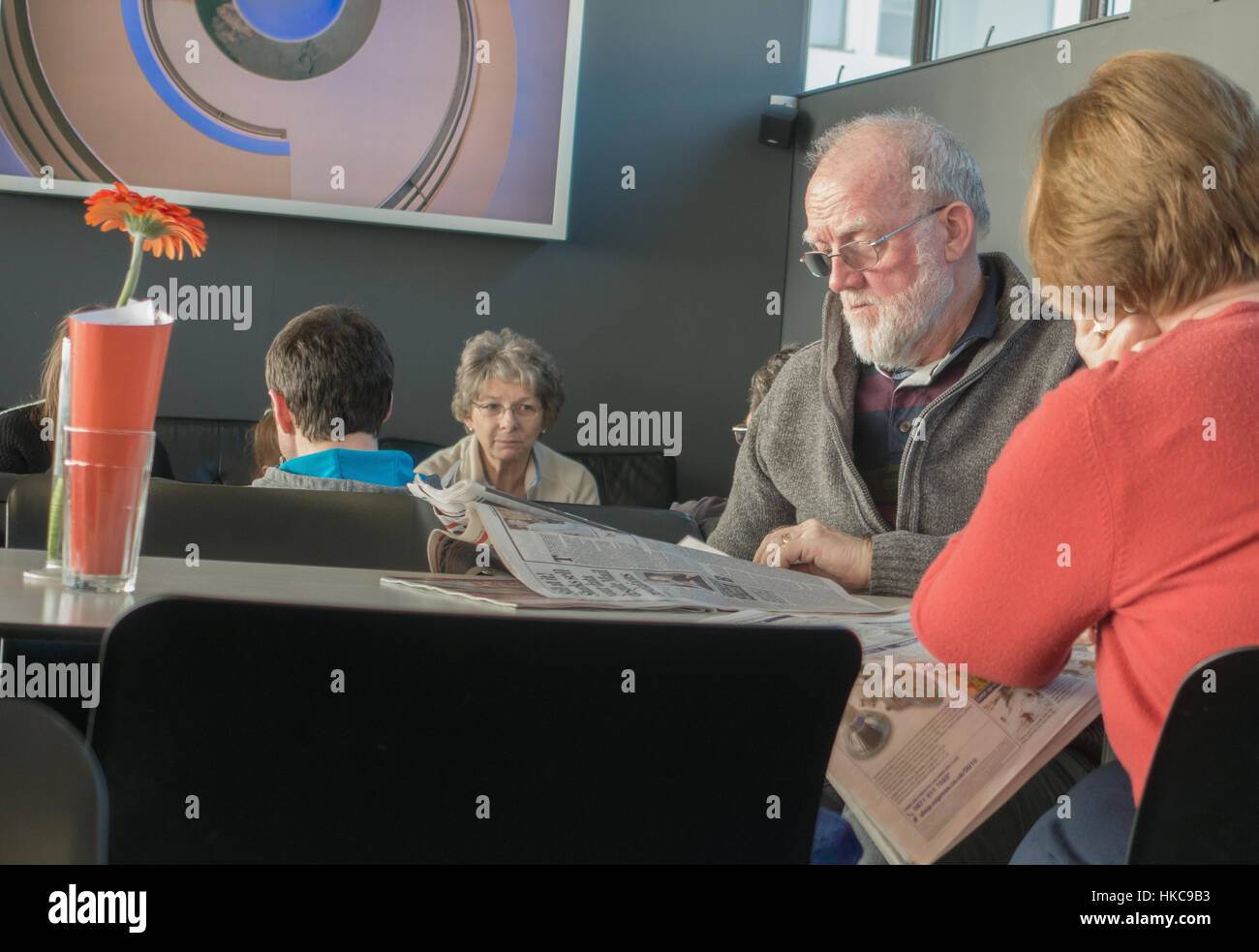 ältere Mann liest Zeitung im Café mit Dame im Hintergrund suchen nachdenklich. Stockfoto