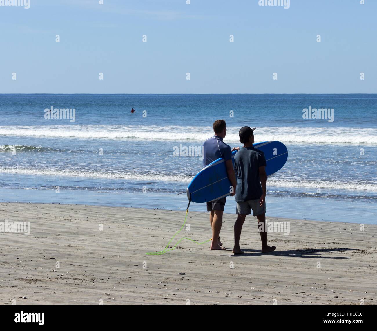Ein Surf-Student trägt seinem Surfbrett auf den Pazifischen Ozean Pausen während seines Lehrers neben geht. Stockfoto