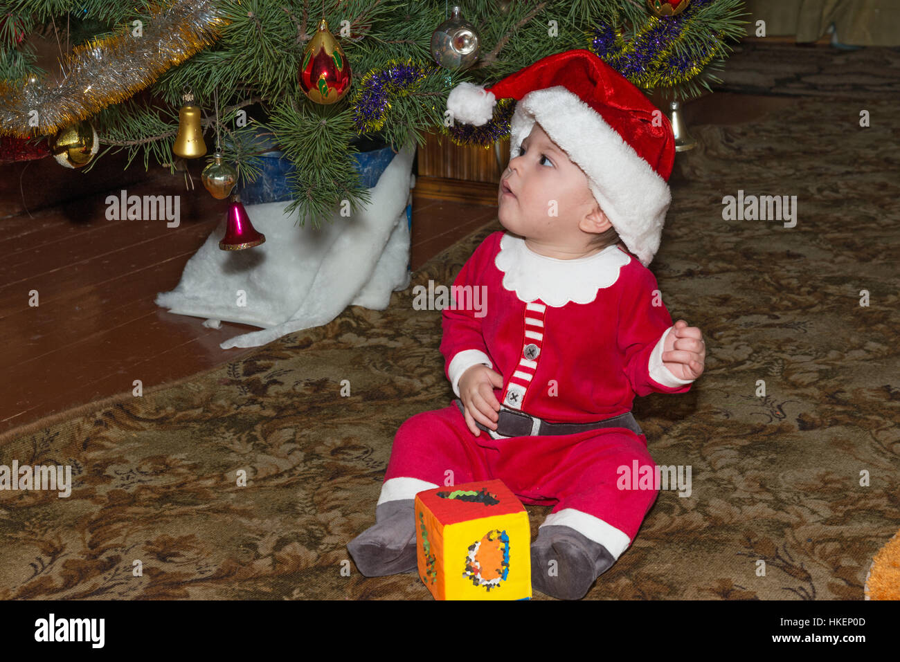 Kleinen Jungen in rot-weiße Weihnachtsmannkostüm sitzt am Boden unter dem Weihnachtsbaum. Stockfoto