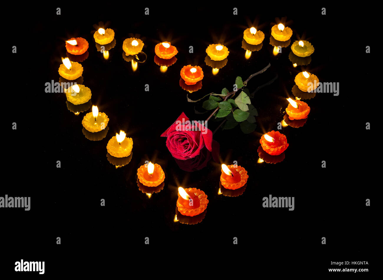 Romantische Valentines Tag Setup mit brennenden Kerzen in Herzform und eine rote Rose auf schwarzem Hintergrund - Liebesbeziehung. Stockfoto
