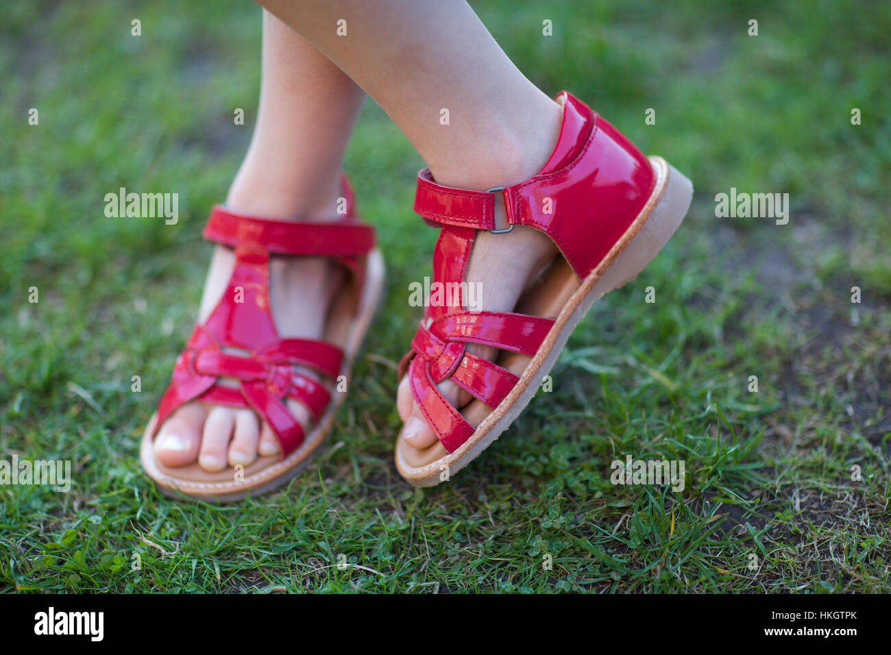 geringer Teil der Mädchen mit gekreuzten Beinen steht. Schuhe, Muster, Rasen, Kind. Stockfoto