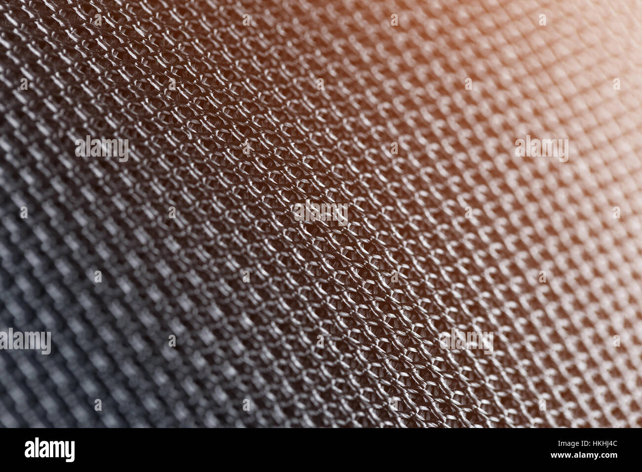 Schließen Sie Fokus auf künstlichen metallischen Oberfläche von schwarz Kunststoff mit soft Orange Licht weben gemacht. Stockfoto