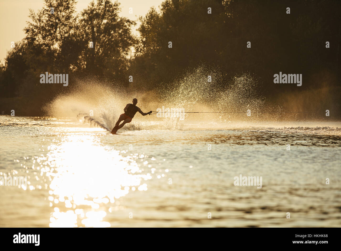 Man Wasserski bei Sonnenuntergang. Mann reitet Wakeboard auf Seewasser. Stockfoto