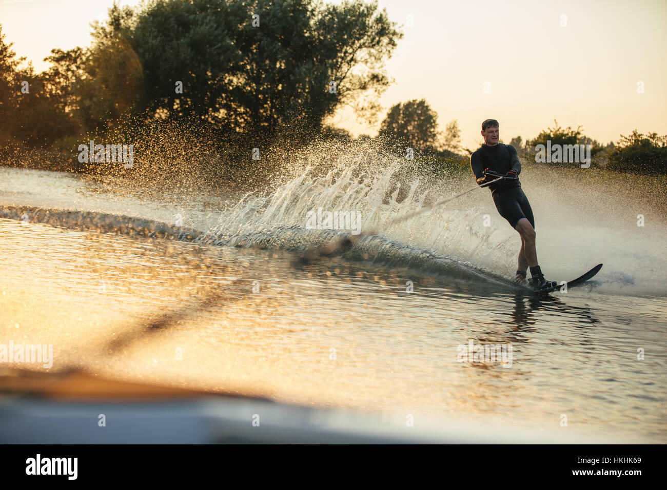 Mann Wakeboarden auf See hinter Motorboot bei Sonnenuntergang. Wasserski auf See. Stockfoto