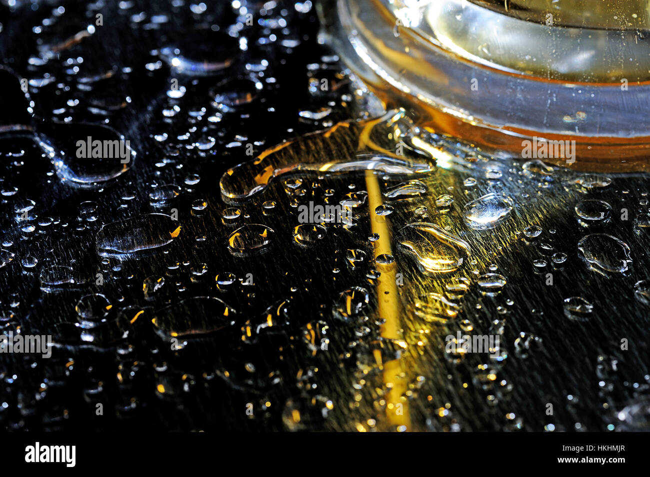 Tropfen des braunen Bieres auf schwarzen nassen Tisch Stockfoto