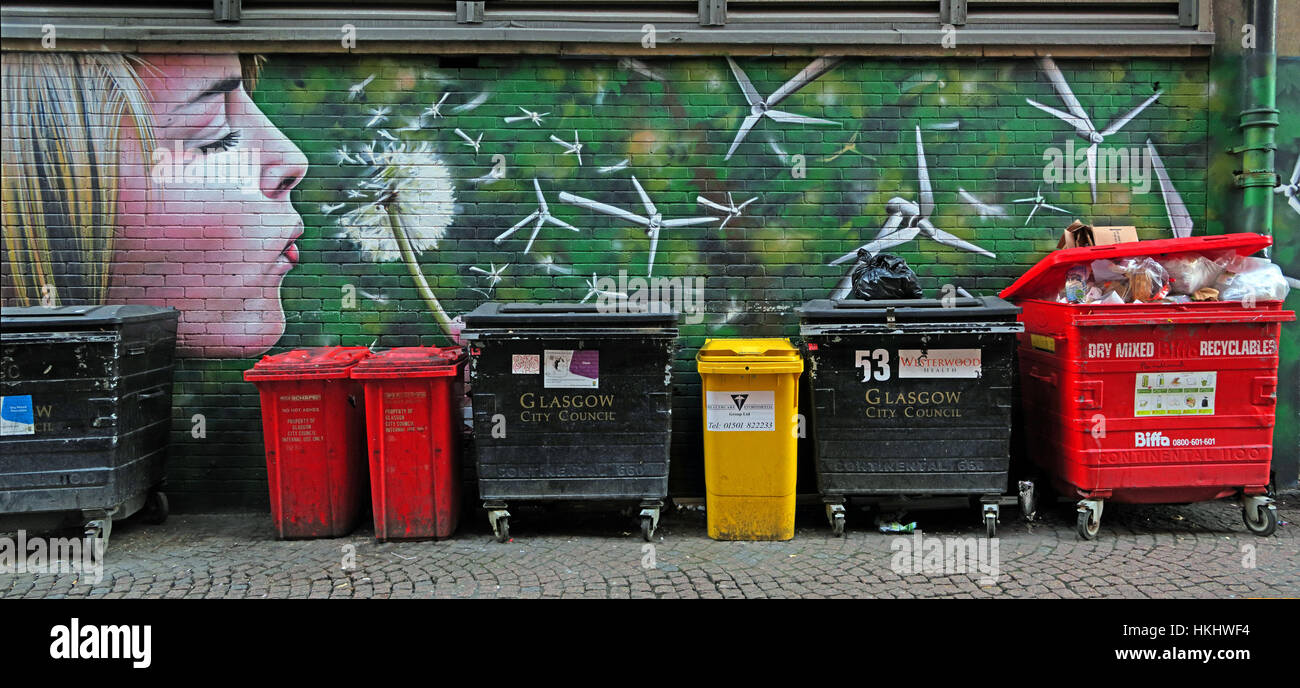 Graffiti in Glasgows Hinterstraße, blonde Frau bläst einen Löwenzahn in Windturbinen, erzeugt grüne Energie, in der Nähe von Mülltonnen Stockfoto