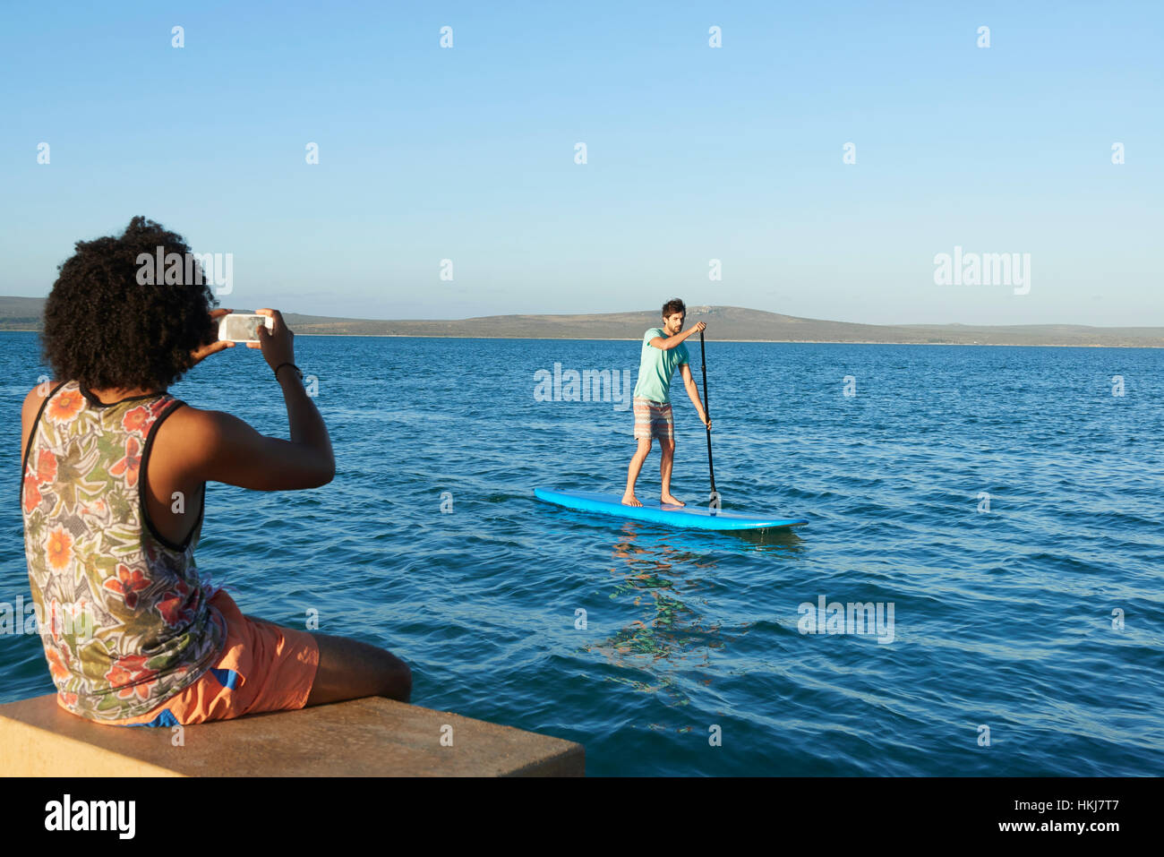 Junger Mann Fotografieren Freund Paddling auf sonnigen Sommer Meer Stockfoto