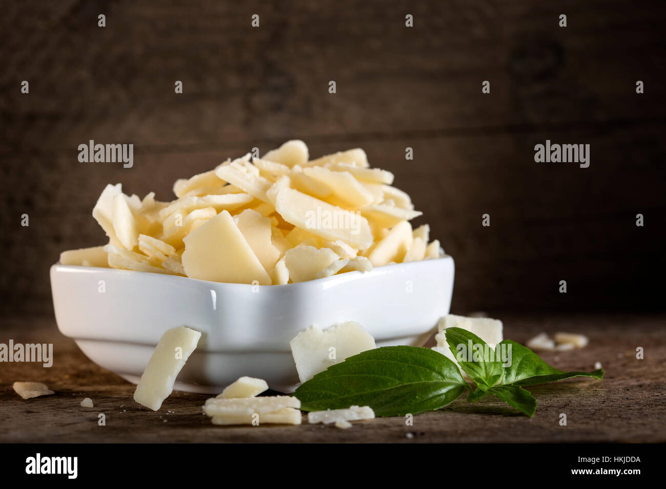 Schüssel mit Parmesan Käse Flocken und Basilikum auf rustikalen Holztisch Stockfoto